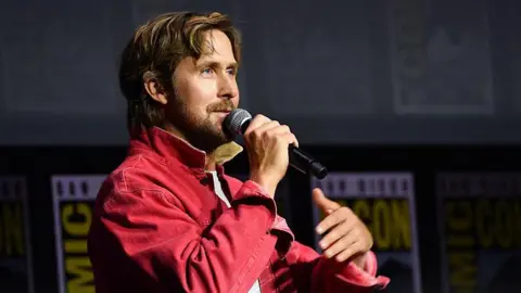 AFP via Getty Images Ryan Gosling speaking into microphone on stage at San Diego Comic-Con