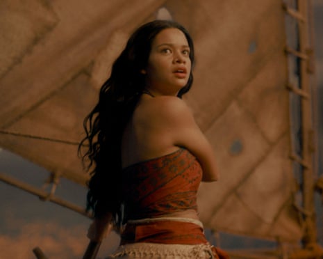 Catherine Laga'aia as Moana in traditional Pacific Island dress looks over her shoulder inside a wooden structure