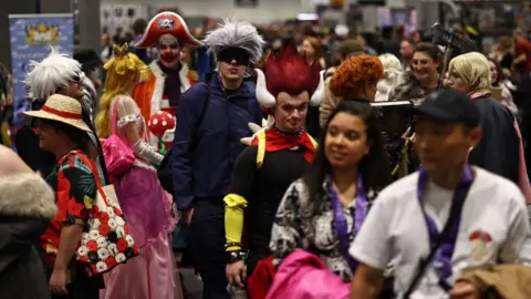 Getty Images Groups of fans, many in colourful costumes, making their way across the floor of a convention