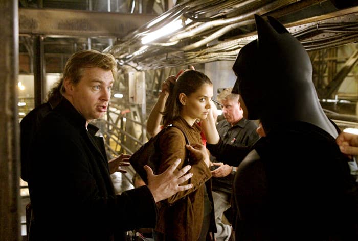 A director is conversing passionately with a woman and an actor in a Batman costume on a film set