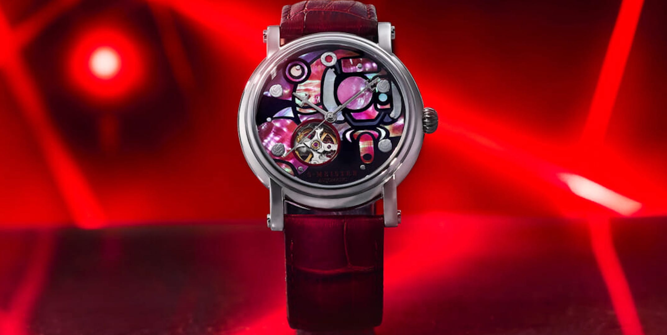 mechanical watch with abstract dial design and red strap against red background