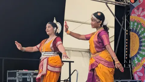 Art Asia Two women in traditional South Asian clothing dance on stage.