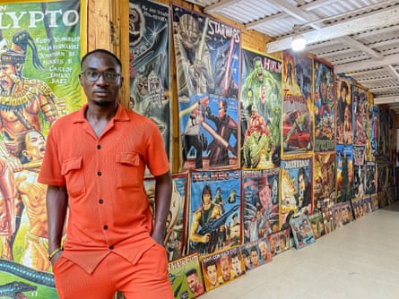 Robert Kofi in front of a wall adorned with hand-painted film posters.