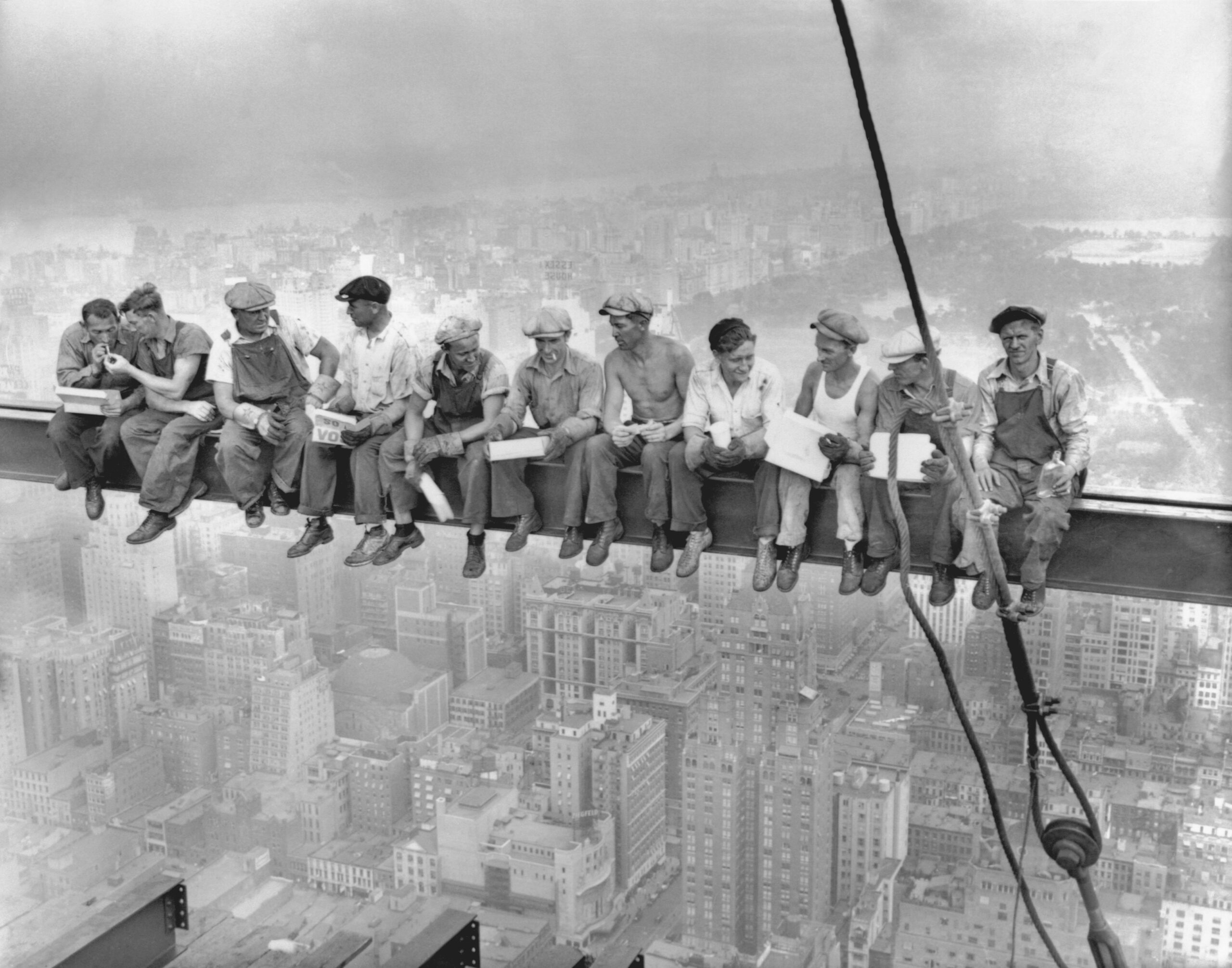 Workers sit on a steel beam high above New York City, eating lunch during the construction of Rockefeller Center in 1932