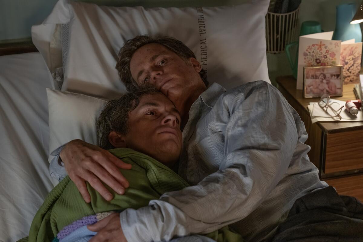 Two men laying on a hospital bed embracing one another.