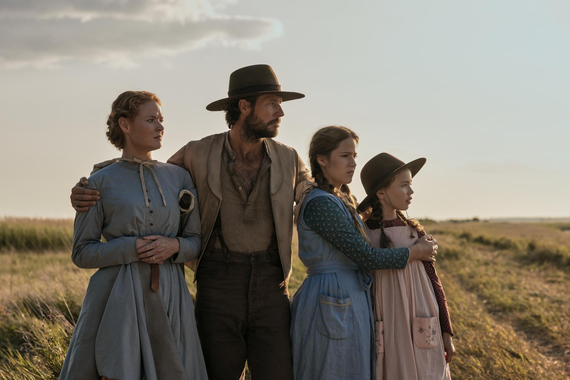 A woman and man standing next to their two young girls on a prairie.