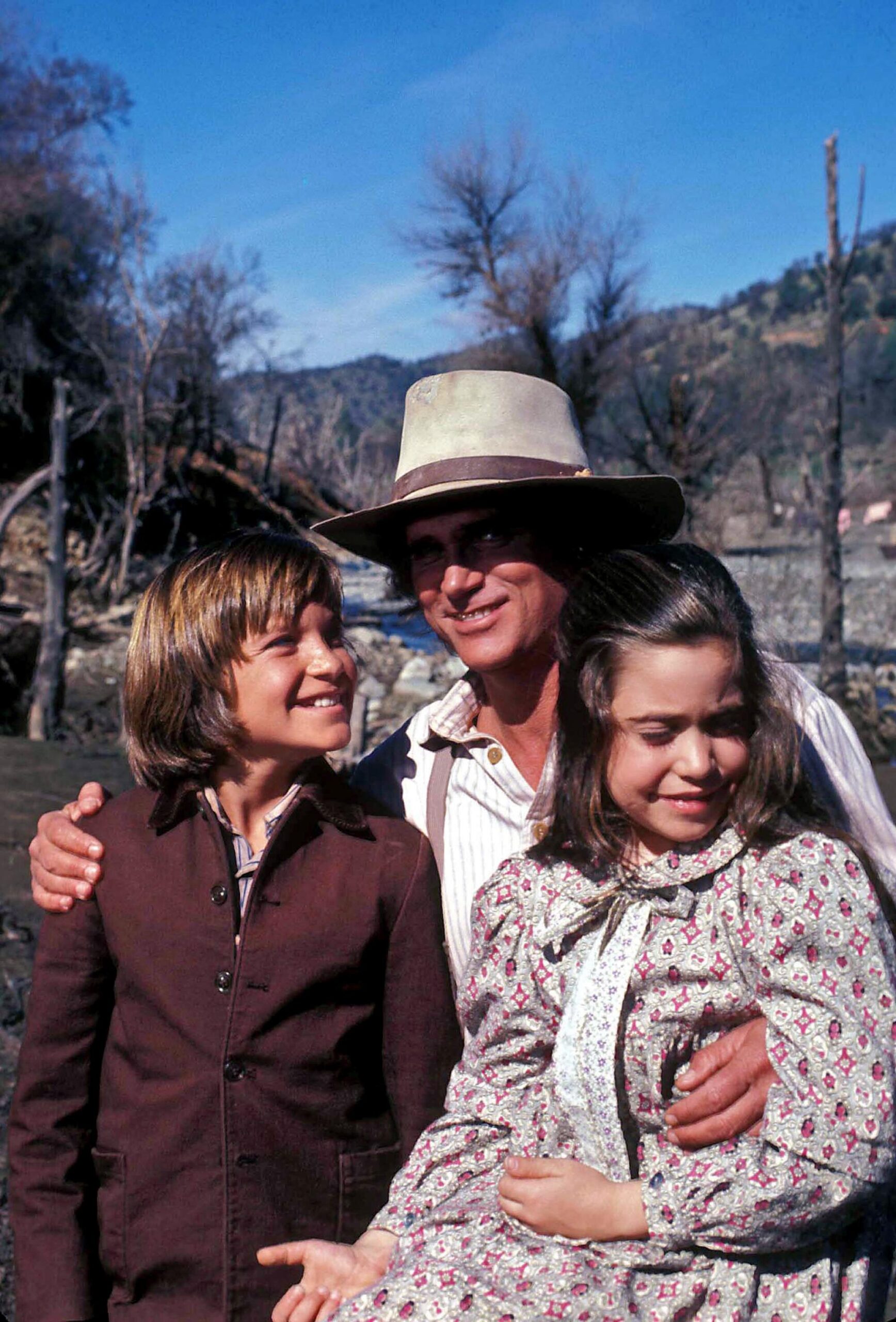 A boy and a girl on each side of a man wearing a dirty tan hat.