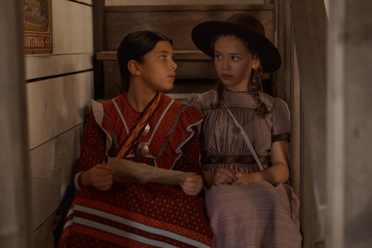 Two girls sit side by side in a stairwell, looking at each other.