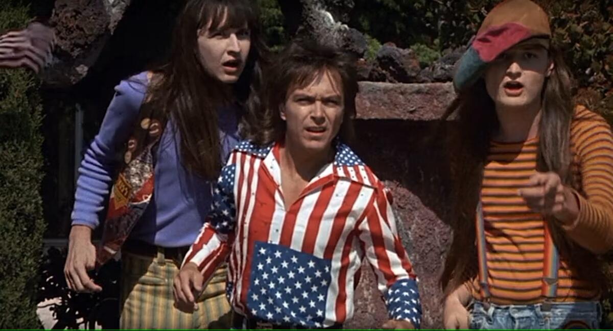 Three people in brightly colored clothing stand with confused looks on their faces.