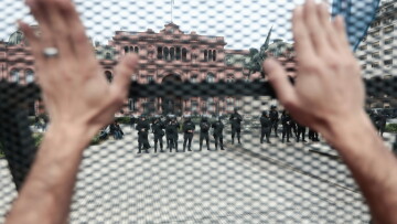 A protester raises his hands behind a fence as security forces stand guard outside Casa Rosada presidential palace in the Argentine capital during a visit of IMF Managing Director Kristalina Georgieva