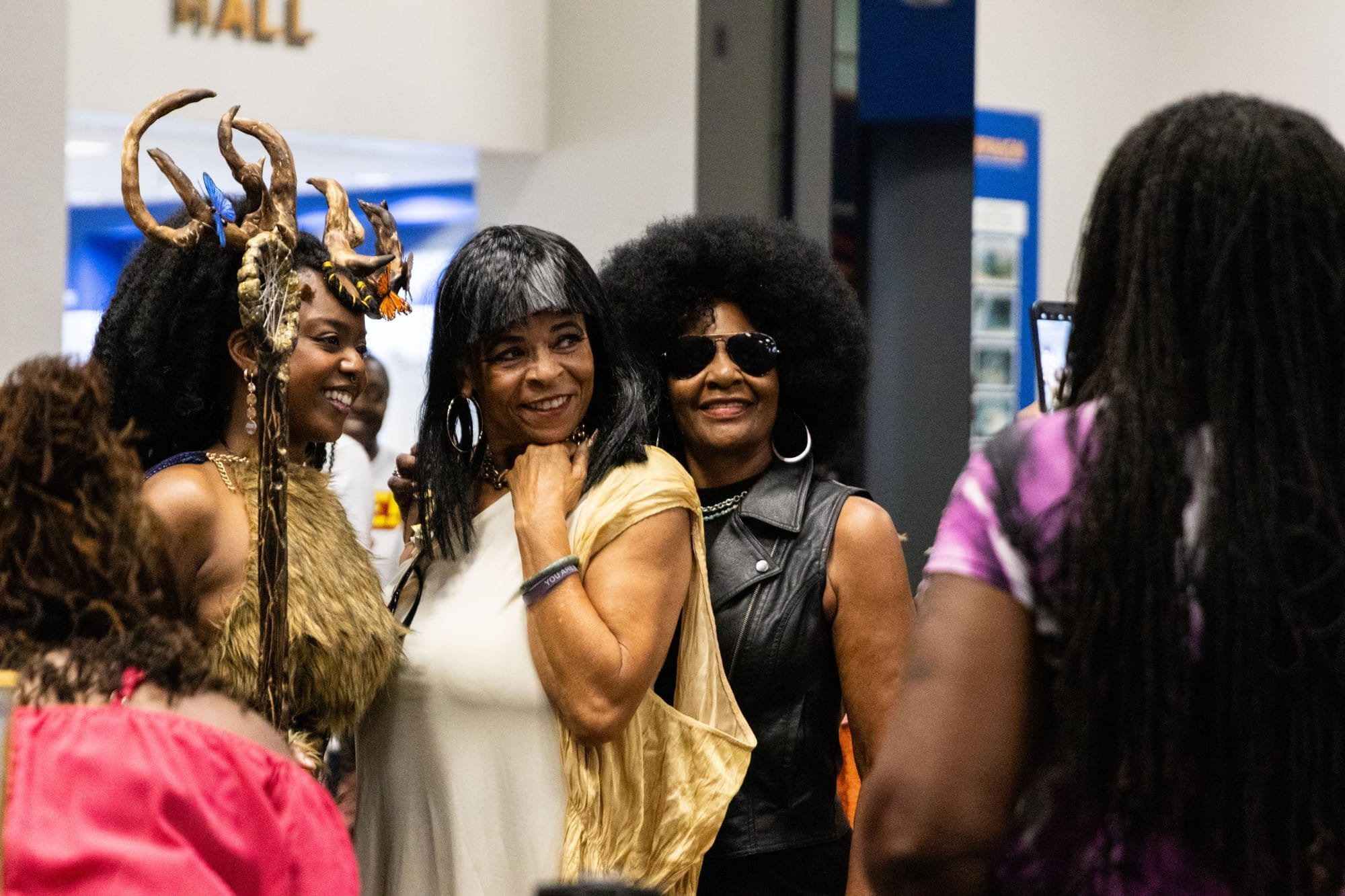 People in cosplay outfits including an afro and deer horns pose for a photograph in a museum