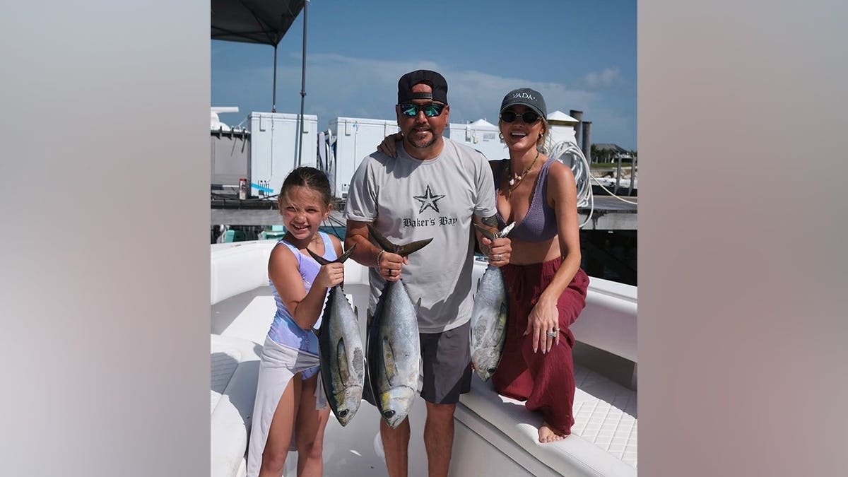 Brittany Aldean smiles alongside husband Jason Aldean and daughter Navy while holding freshly caught fish aboard a boat in the Bahamas.