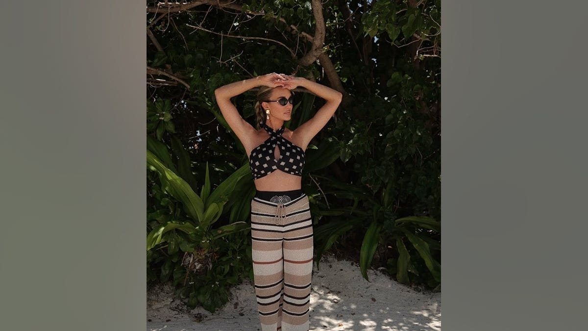 Brittany Aldean poses among tropical greenery while wearing a black geometric-print halter top, striped knit pants and oversized sunglasses during a Bahamas getaway.