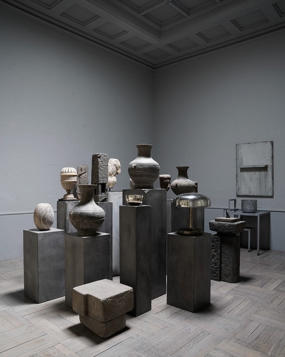 Collection of ancient pottery and stone artifacts displayed on pedestals in a dimly lit museum gallery.