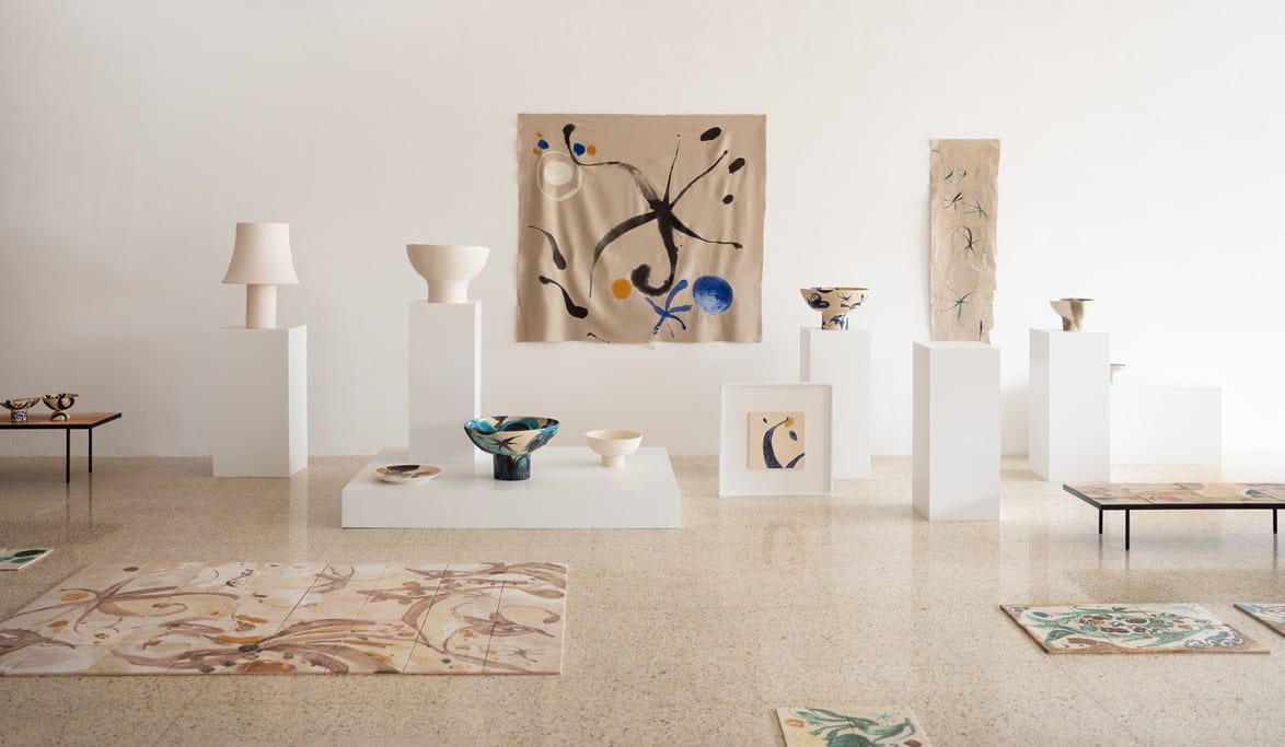Art gallery display with pottery and abstract paintings on white pedestals against a light-colored wall.