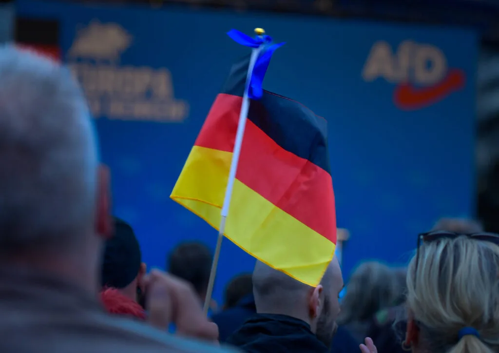 A German flag is pictured in the hand of a crowd member in front of a photo wall at an AfD rally on the Schlossplatz Oranienburg on May 6, 2024.