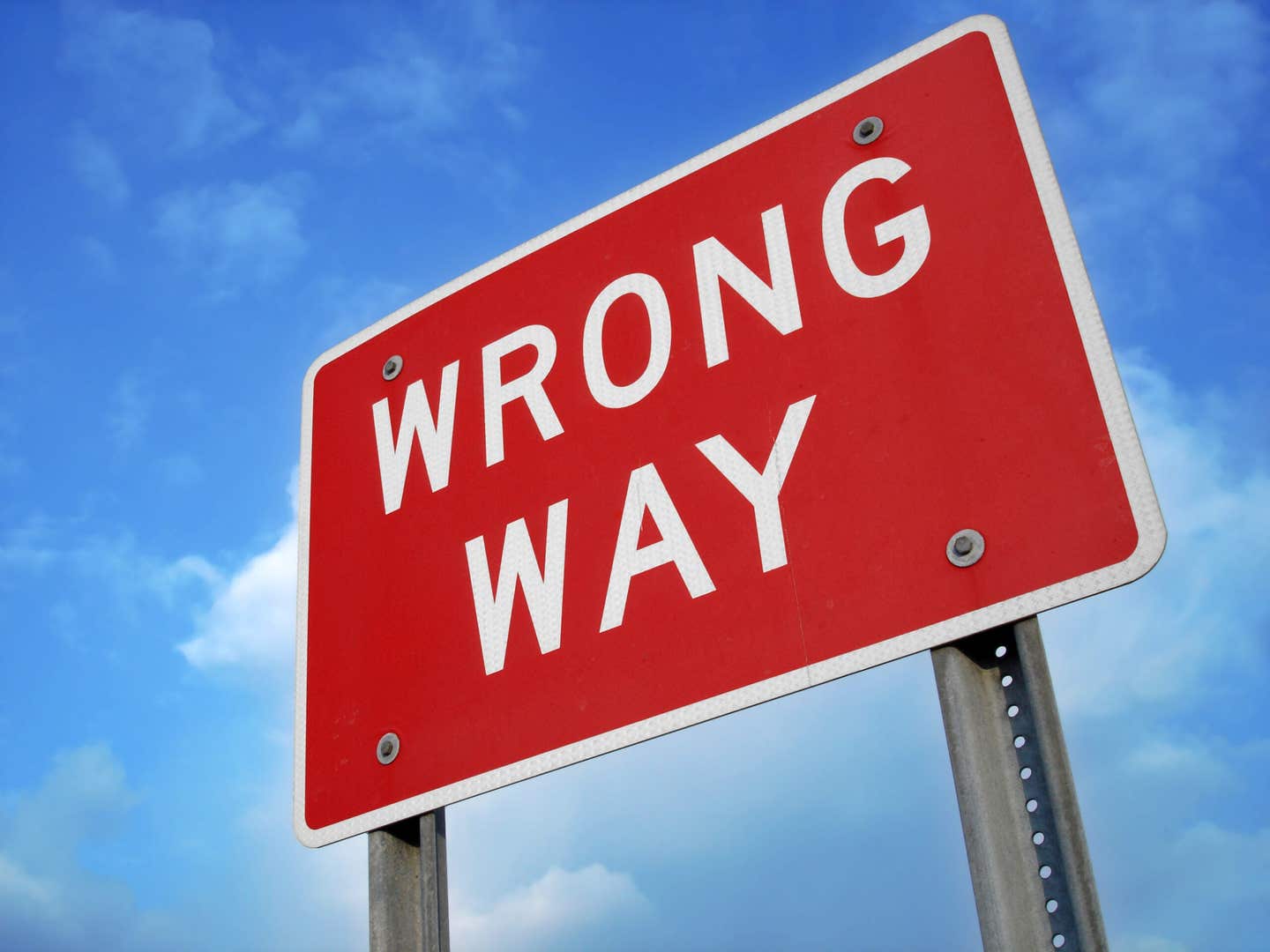 Wrong way sign at angle against blue sky with clouds.