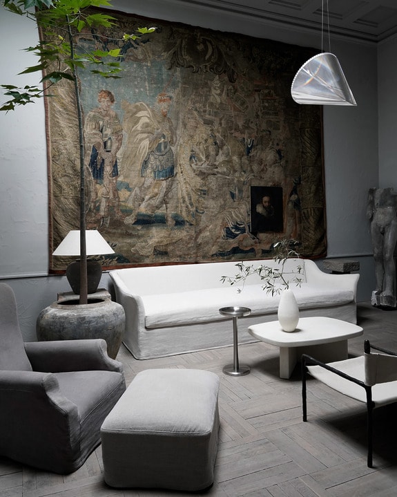 Elegant living room with gray chairs, white sofa, tall plant, large tapestry on wall, pendant light, and modern coffee table.