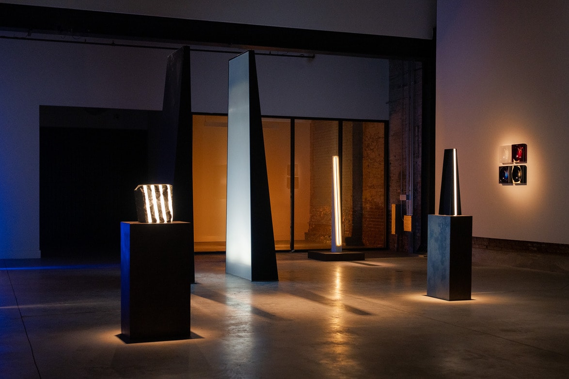 Modern art installation in a dimly lit gallery with geometric light sculptures on display.
