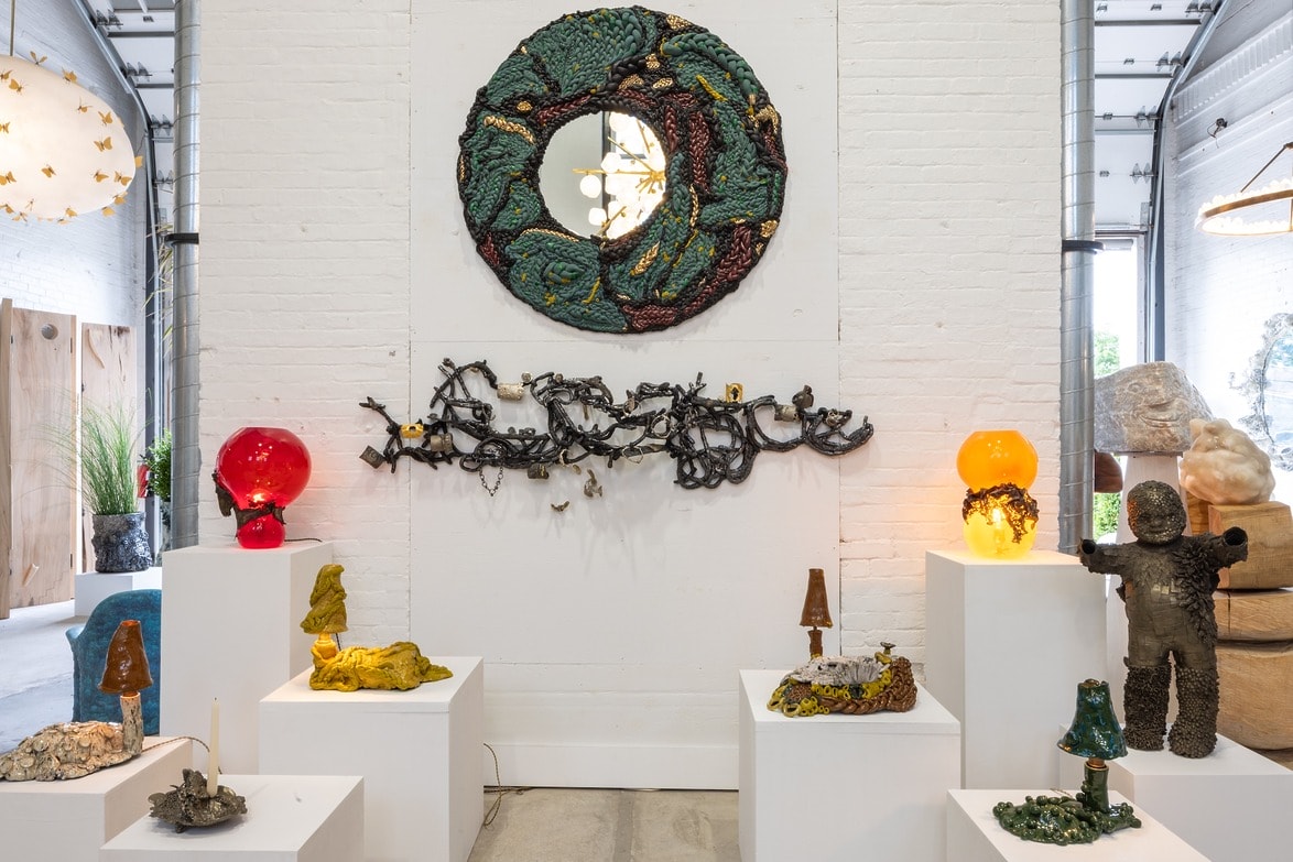Art installation with circular wall sculpture, abstract elements, and colorful sculptural pieces on pedestals in a gallery setting.