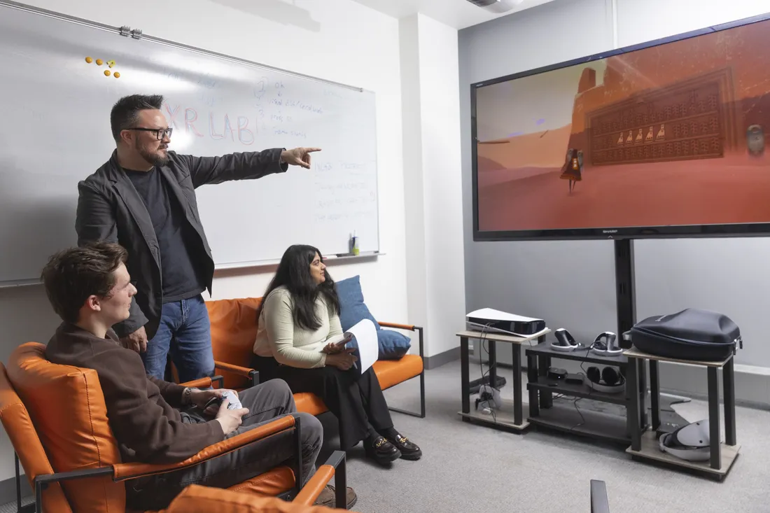 Professor Nick Bowman standing with two students and pointing at a television screen.