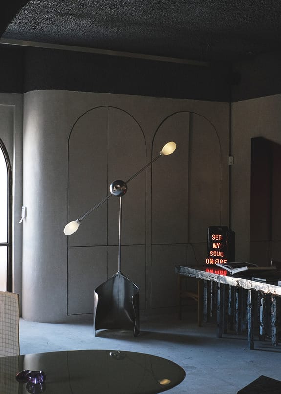 Modern interior with unique standing lamp, arched wall design, and a neon sign in a dimly lit room.
