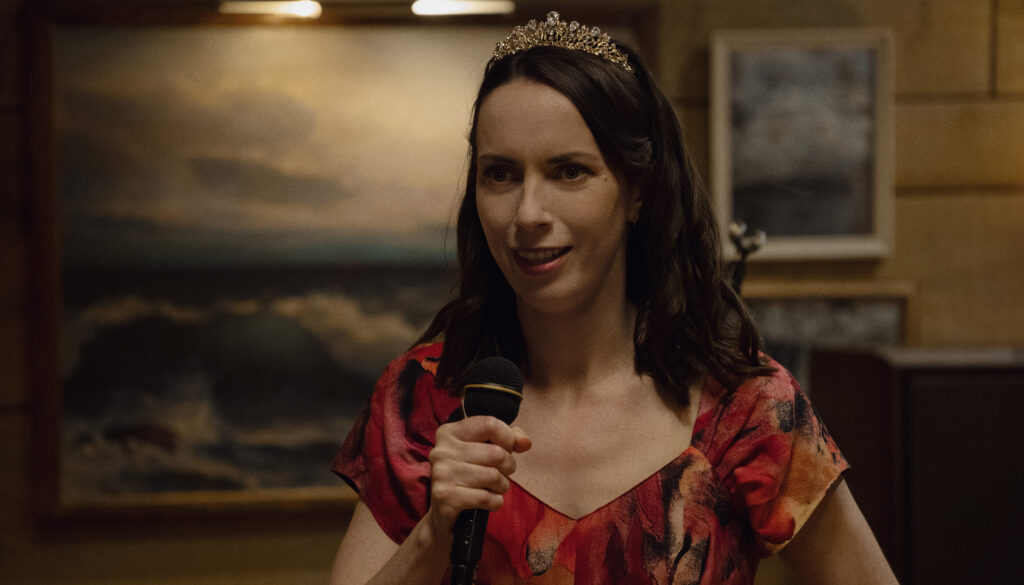 Widow's Bay character Patricia wearing a tiara and holding a microphone, radiating a relatable mixture of awkward anxiety and determination.