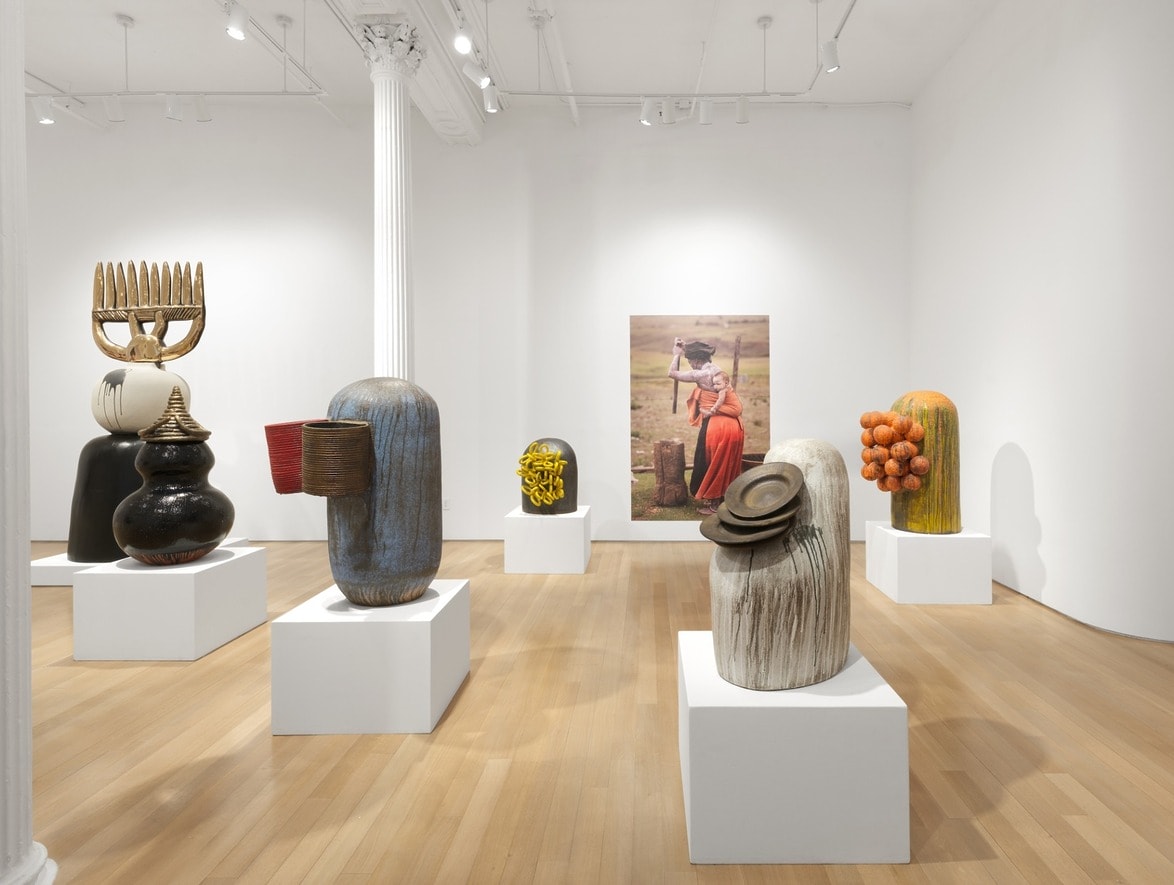 Art gallery interior displaying contemporary sculptures on pedestals with white walls and wooden floor.