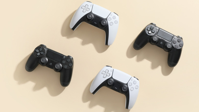 Four PlayStation controllers arranged on a light background, featuring two white DualSense controllers alongside two black DualShock 4 controllers.