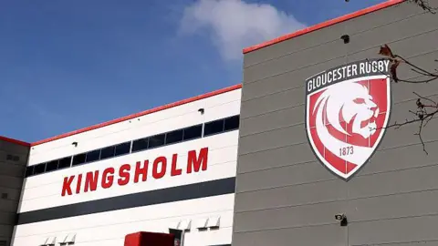 Getty Images A general view of the exterior of Gloucester Rugby's Kingsholm stadium with the word "Kingsholm" in large red letters on a white background and the club's badge showing a white lion on a red background