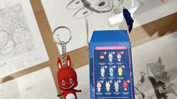 A red labubu doll on a keychain, with its box next to it