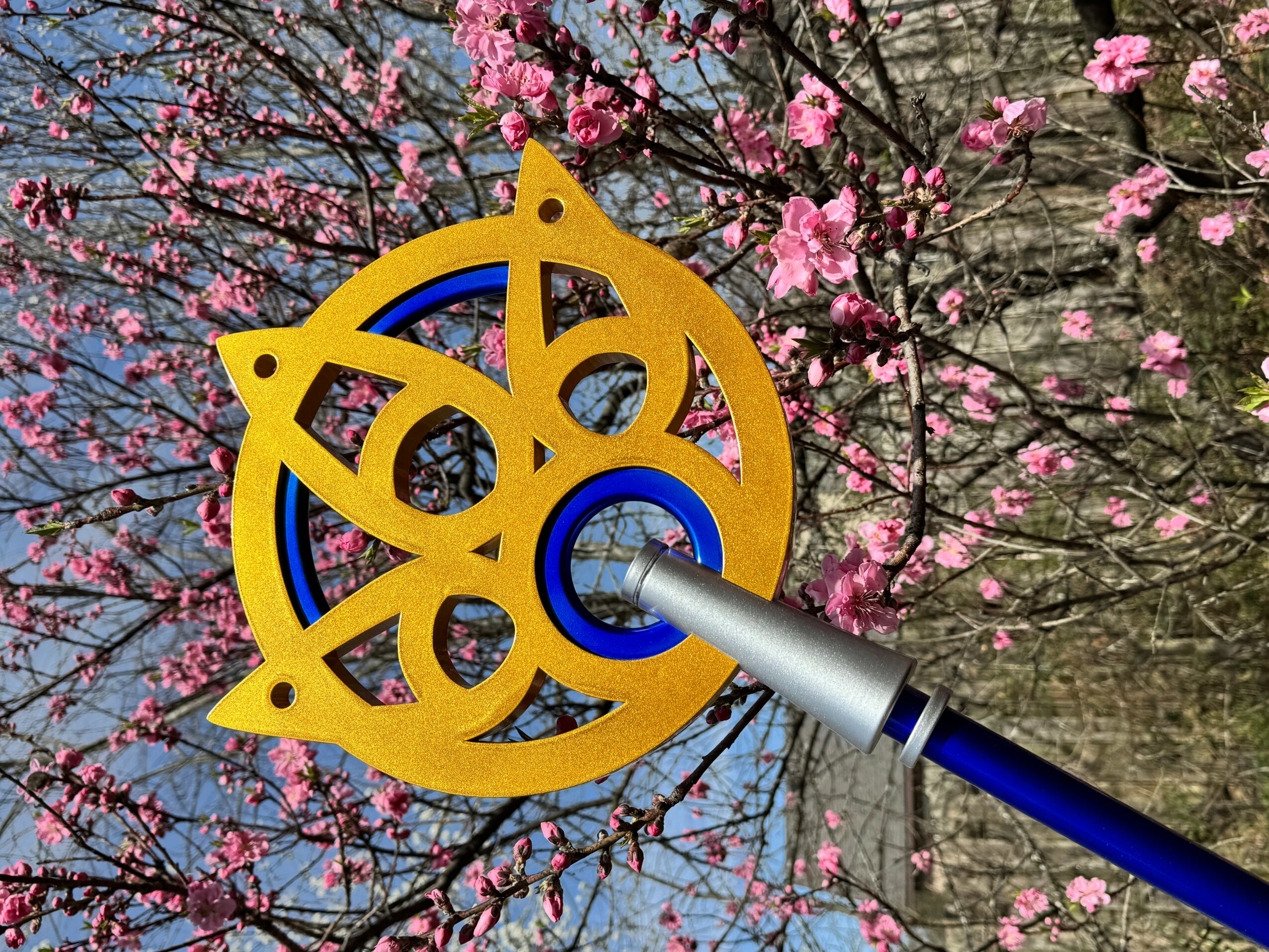 A yellow and blue mechanical tool attached to a pole, with pink flowering trees in the background.
