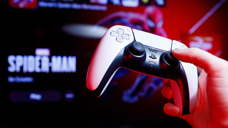 A DualSense controller in front of a screen displaying the PlayStation 5's home menu.
