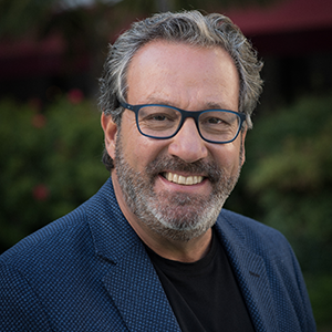 A bearded man in glasses wearing a blue blazer over a plain black t-shirt