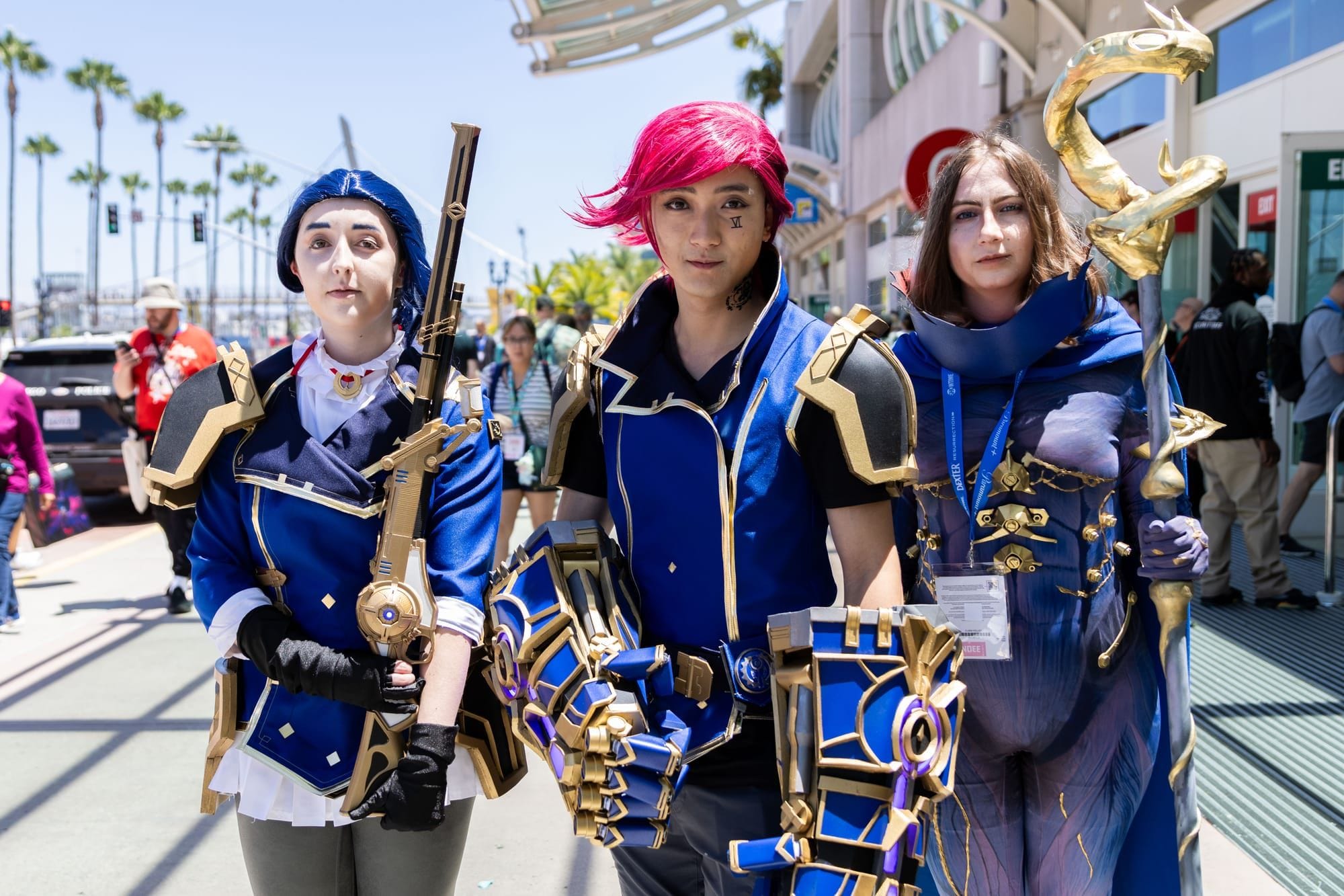 People in blue and purple cosplay outfits stand in front of a convention center with palm trees in the background