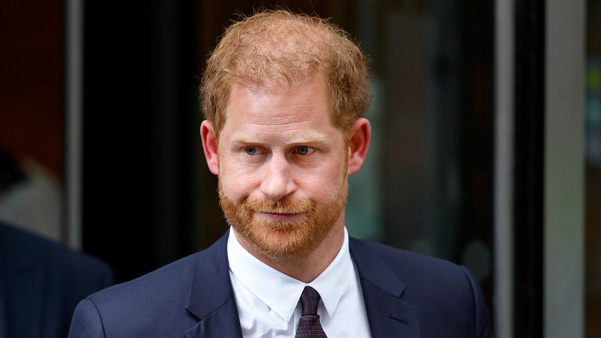 A close-up of Prince Harry looking serious in a dark suit, white shirt and black skinny tie.