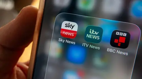Getty Images Hand holding a phone, that shows ITV and Sky and BBC news apps on the phone screen.