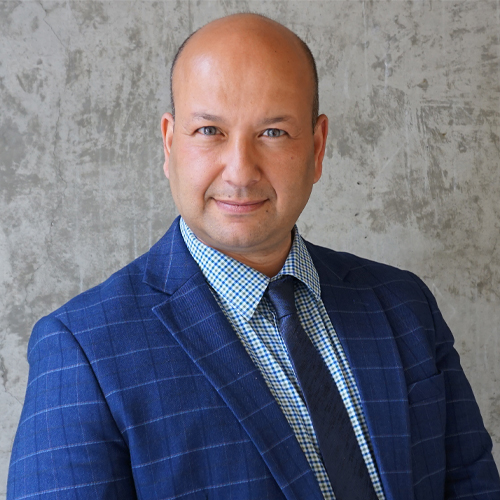 A man wearing a blue, checkered suit jacket and tie over a blue dress shirt