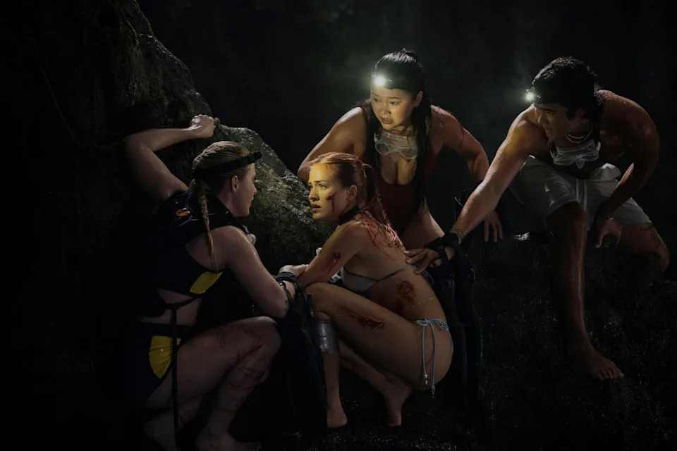 Kathryn Newton, Tommi Rose, Lana Condor and Nico Hiraga in The Devil's Mouth. Three young women and a young man crouch in the dark near a large rock. They are wearing swimsuits and head torches.