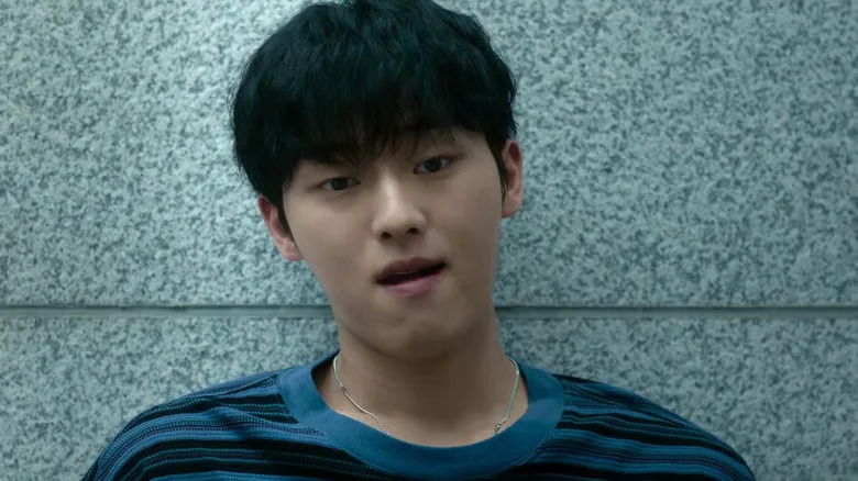 Kang leaning to the wall and looking intrigued