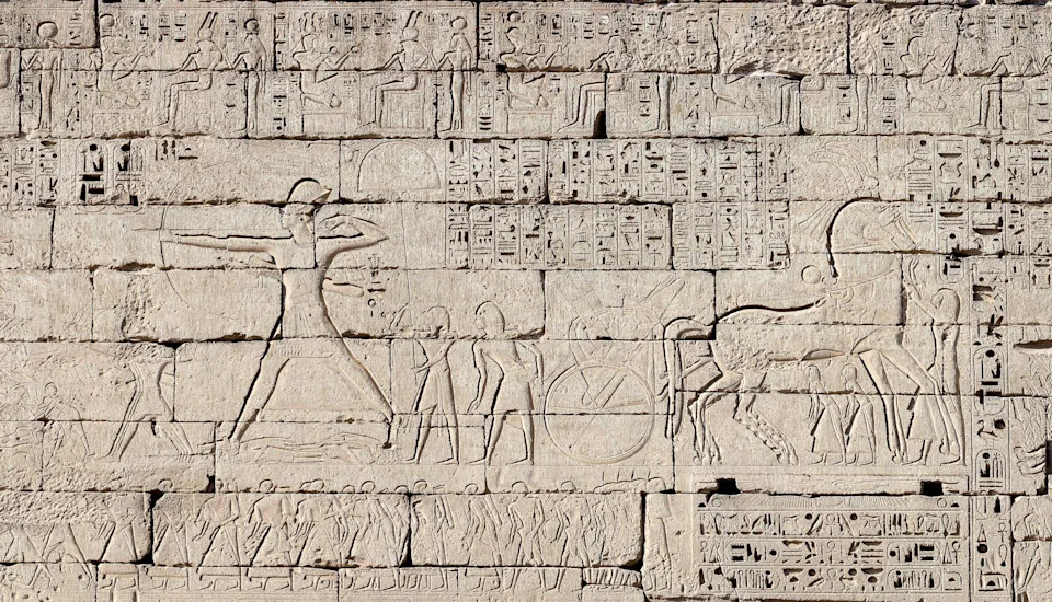 Ancient stone relief showing figures and hieroglyphics, depicting a historical scene with human and animal figures