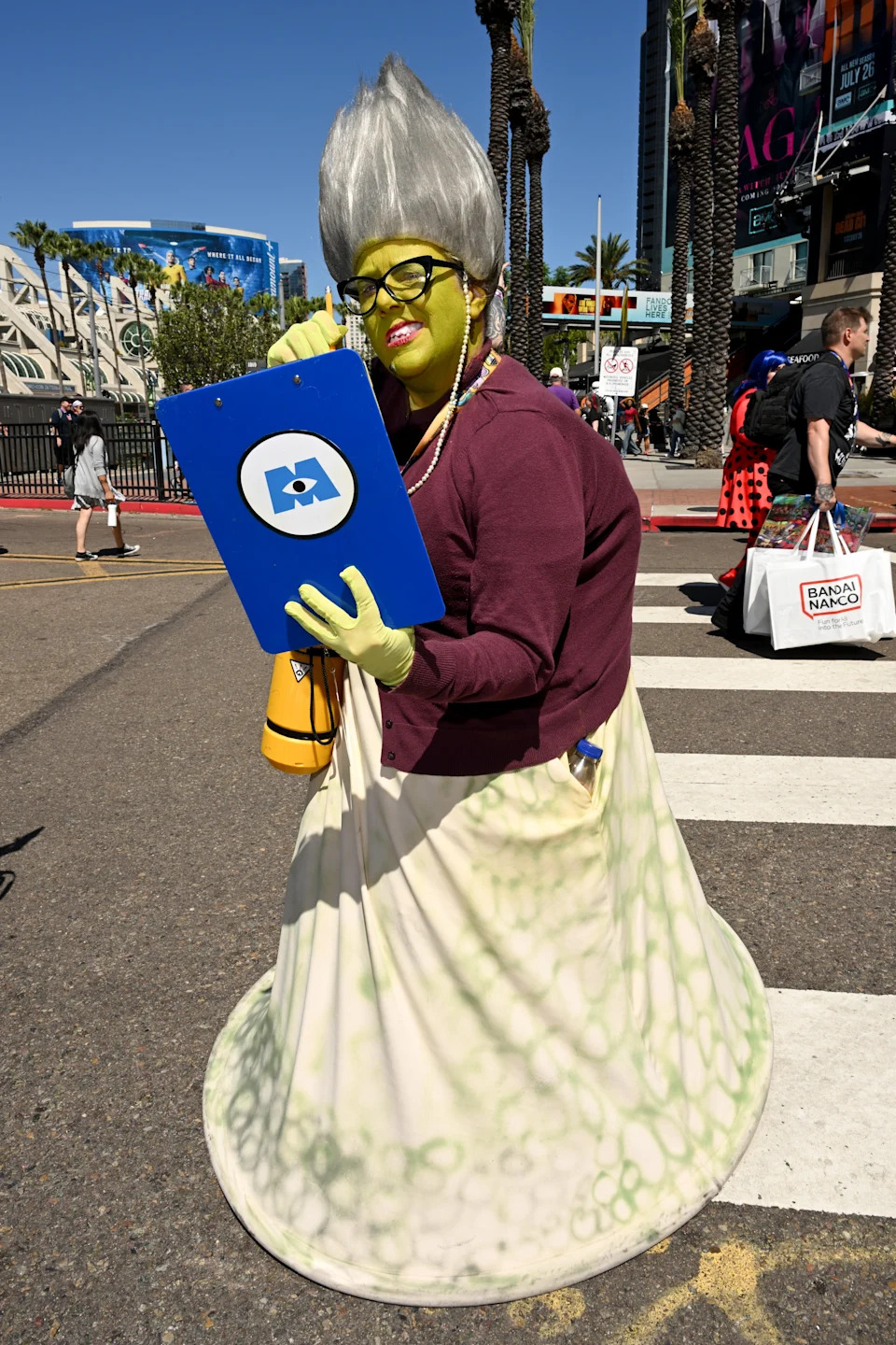 Person in costume with pointed wig, green face paint, holding blue clipboard, crossing a street at a convention