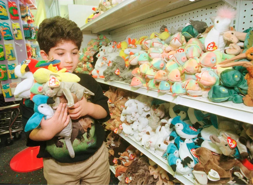 A young boy holds a stack of Beanie Babies while shopping at a toy store filled with shelves of the popular stuffed animals