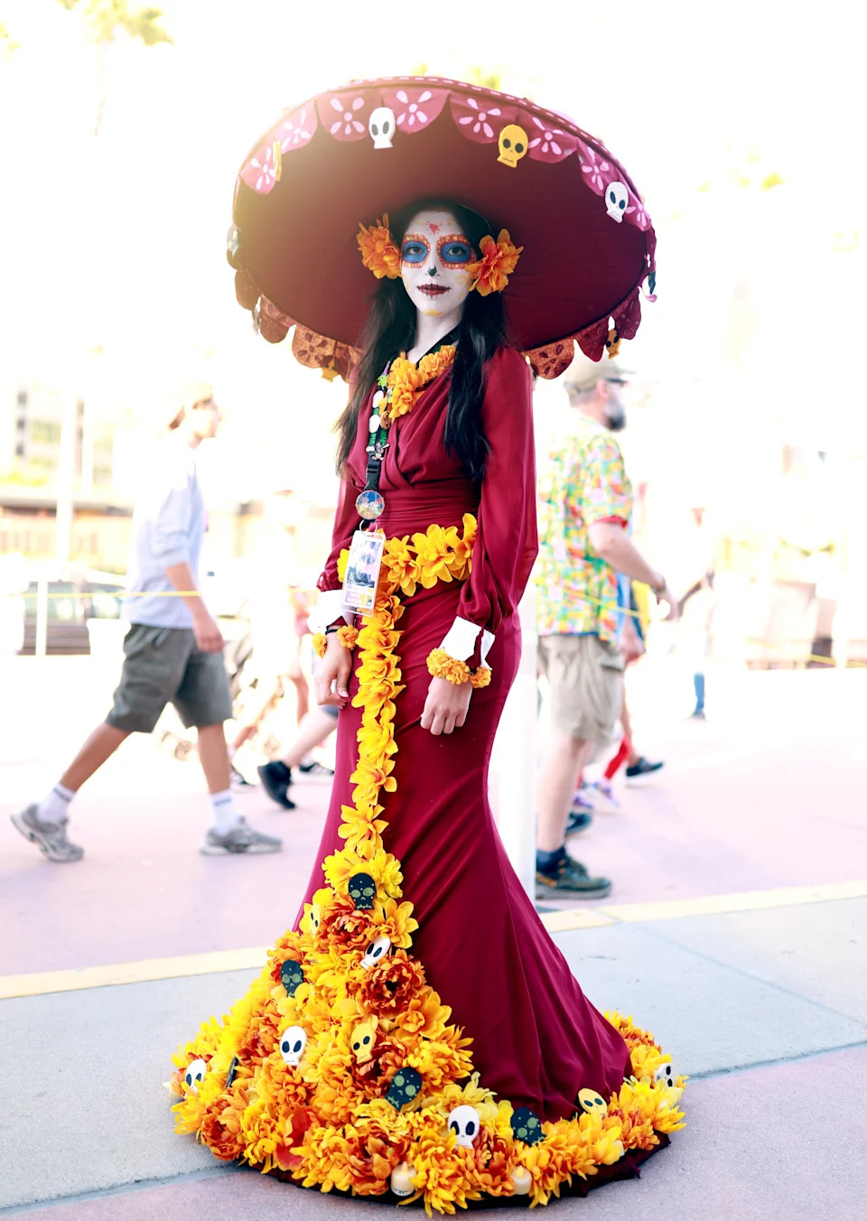 Person wearing an elaborate Day of the Dead costume with a large ornate hat and flower decorations at an outdoor event