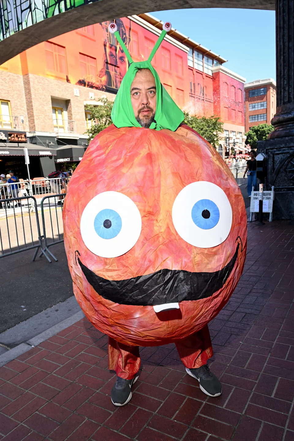 Person in a round, cartoon-style, orange costume with large eyes, mustache, and green antennae on their head, standing outdoors