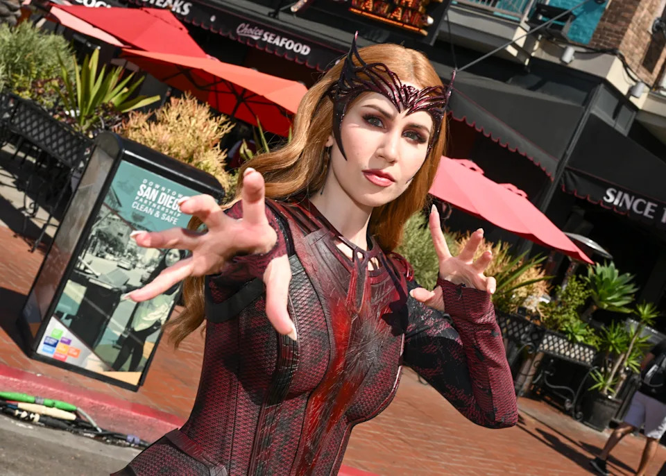 Person in a detailed superhero costume posing dramatically outdoors, with hands extended toward the camera