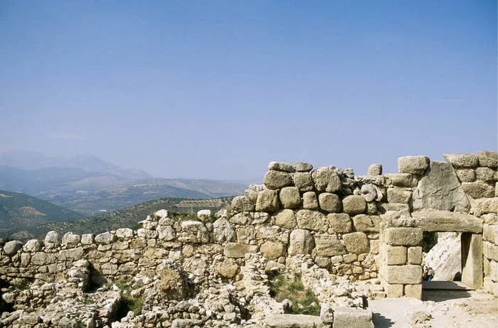 Ancient stone ruins with a doorway, set against a mountainous landscape under a clear sky