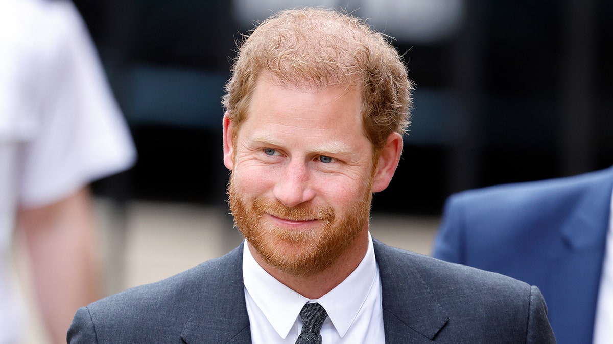 A close-up of Prince Harry smirking in a dark suit.