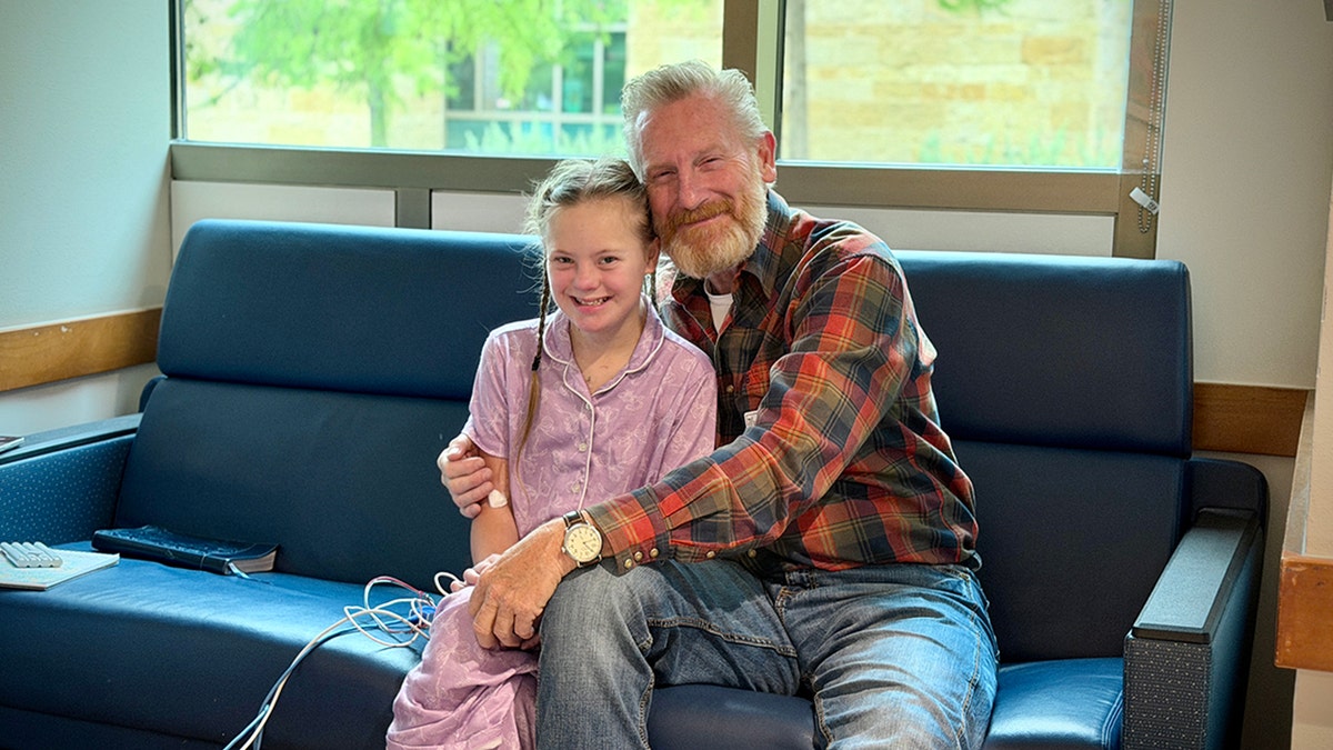 Rory Feek sits with his youngest daughter Indiana on a blue couch indoors.