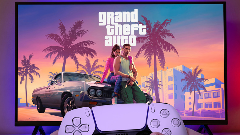 Hands holding a PlayStation 5 DualSense controller with the GTA 6 artwork on a TV screen in the background